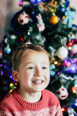 joyful and cute boy of European appearance near the Christmas tree in the room selective focus