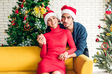 Romantic sweet couple in santa hats having fun decorating christmas tree and smiling while celebrating new year eve and enjoying spending time together in christmas time at home