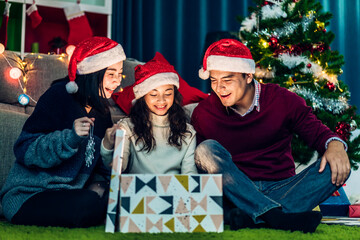 Portrait of happy family father and mother with daughter in santa hats having fun opening magic christmas gift box and enjoying spending time together in christmas time at home.