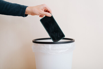 Close-up of person throwing mobile phone into trash can. Rejection of technology, outdated or broken smartphone