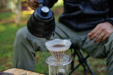 A man making drip coffee with a beautiful nature view in background. Drip brewing filtered coffee or pour-over is a method involves pouring water over roasted ground coffee beans contained in filter.