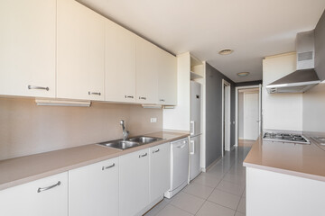 Beige interior of a spacious kitchen with tiled floors, granite countertops with a built-in sink...