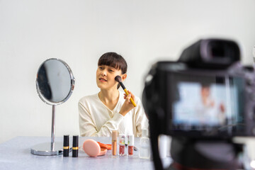 Young female blogger reviewing and recording vlog video on camera screen with makeup cosmetic at home.
