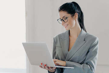 Self confident cheerful woman economist analyzes report about company income on laptop computer,...