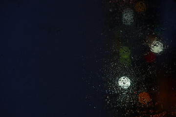 Raindrops on a window glass and unfocused lights of a night or evening city. Background of night city behind the glass during rain