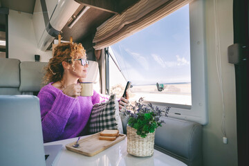 One tourist woman admire the beach inside her modern camper van and use mobile phone. Summer...