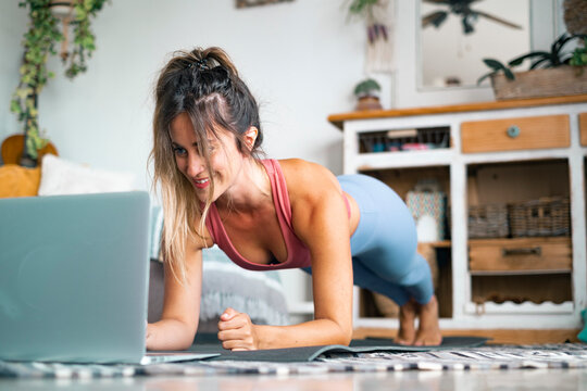 Healthy sport fitness lifestyle at home using laptop to watch and follow online lessons. Cheerful woman on the floor doing push ups plank exercise to build a perfect healthy body alone. Workout people