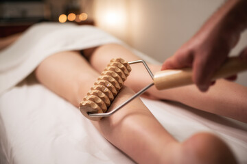 Wooden roller tool for anti cellulite massage. Massaging legs - obrazy, fototapety, plakaty