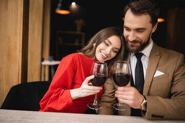 cheerful woman and bearded man clinking glasses with red wine during celebration on valentines day