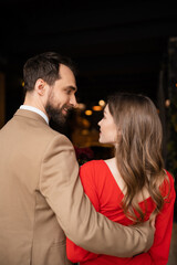 happy and bearded man hugging cheerful girlfriend in red dress on valentines day