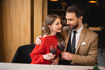 positive woman clinking glasses of wine with bearded man on valentines day
