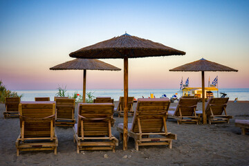 Fototapeta premium Colorful sky over sunshades with loungers on sandy beach at resort Faliraki in Rhodes island