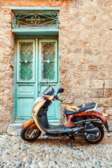 Old moped parked in front of typical mediterranean stone building with blue doors