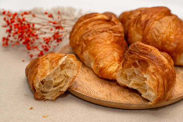 Croissants lie on a wooden textured plate on a jute textured napkin. French traditions.