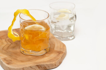 Two embossed  glasses with water and lemon stand on a wooden stand on a white table.