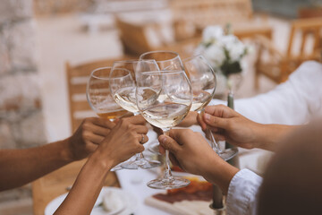 Dinner wood table, hand of friends clinking glasses of white wine, warm toning