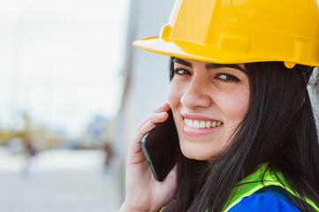 closeup of young engineer woman talking on the phone looking at the camera smiling, copy space.