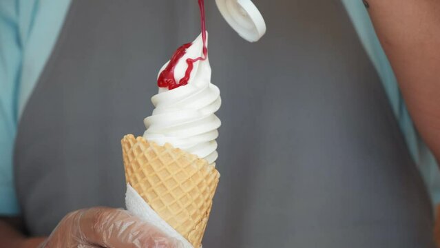 A close-up shot of the chef and the decoration of the ice cream with strawberry topping. yogurt ice cream in a waffle cone with strawberry topping