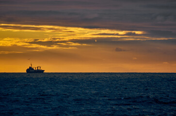 Silhouette of a fishing ship on the horizon of the sea against the backdrop of a dramatic sunset...