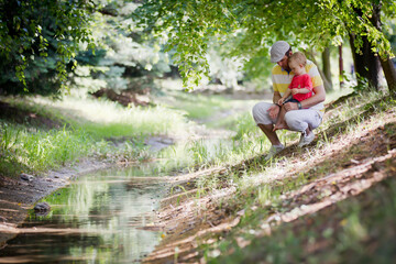 little boy with his father having fun on a bank of a stream during hot summer day