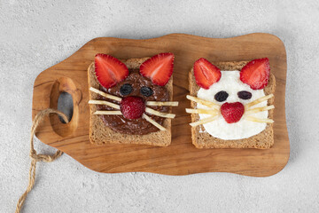 Two sweet toasts for kids in shape of cat with strawberries, banana, cream cheese and chocolate on...