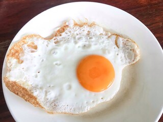 Abstract photo of fried egg in sunny-side-up eggs server in white plate on wooden table 
