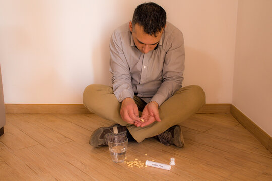 Image of a man sitting on the floor at home taking psychiatric drugs such as anti-anxiety and antidepressant drugs. Drug dependence and addiction.
