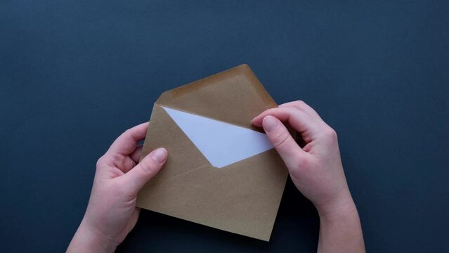 Woman's hand opening a craft mail envelope and take a blank paper on a dark table top view