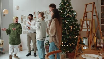 Laughing multinational friends celebrating Christmas and dancing near Christmas tree at home - Powered by Adobe