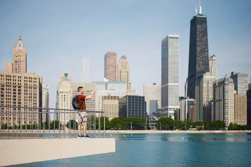 Tuinposter View of Chicago skyline with skyscrapers. Selective focus on young man while photographing cityscape with smart phone.. © Chalabala