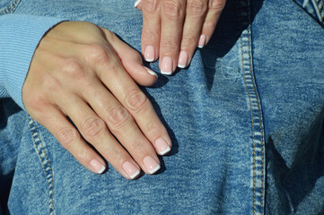 Hands with a professional manicure on the background of a denim jacket. Well-groomed female...