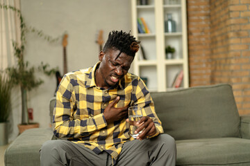 Fototapeta premium Sick man at home. Young African man sitting on sofa feeling unwell.