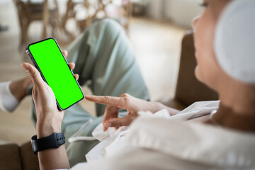 A woman uses a green screen phone on her hand, touches the display and presses a button in the application