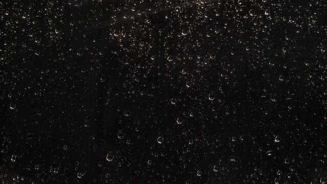Rainy background. Drops of Night rain water flow down the black glass. The drops are illuminated and sparkle