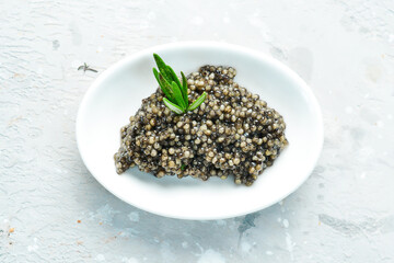 Black caviar in a white bowl. Macro photo. On a gray concrete photo. Side view.