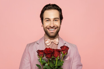 Portrait of positive host of event holding roses and looking at camera isolated on pink