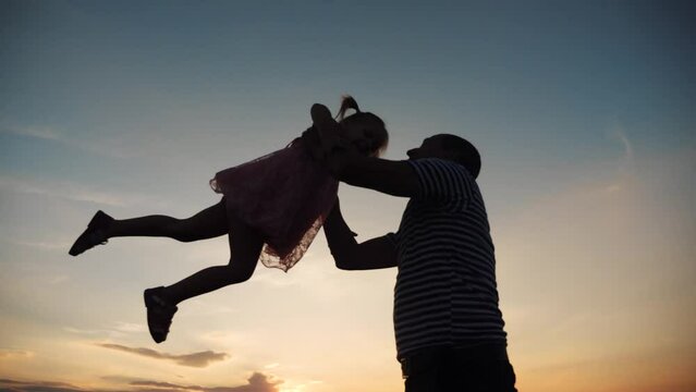 Father and daughter. dad play with his daughter at sunset in the park silhouette throws up. happy family kid dream concept. father and daughter play in the park at dream fun sunset