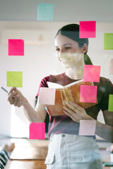 Young smiley attractive, businesswoman using post it notes in glass wall to writing strategy business plan to development grow to success