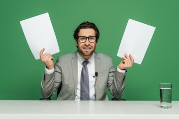 emotional news anchor in eyeglasses and suit holding blank papers isolated on green