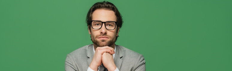 broadcaster in eyeglasses and grey suit with clenched hands isolated on green, banner