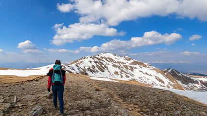 Naklejka premium Rear view of woman with backpack looking at snow capped mountain peak Zirbitzkogel and Kreiskogel, Seetal Alps, Styria (Steiermark), Austria, Europe. Hiking trail Central Alps in sunny early spring