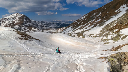 Woman with backpack sliding down on snow covered hiking trail with panoramic view on snowcapped mountain peak Kreiskogel, Seetal Alps, Styria (Steiermark), Austria, Europe. Remote nature in mur valley