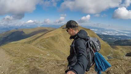 Fototapeta premium Man with backpack and hat taking selfies with panoramic view of the mountain ranges of Zirbitzkogel Grebenzen, Seetal Alps, Styria (Steiermark), Austria, Europe. Idyllic hiking trails in sunny summer