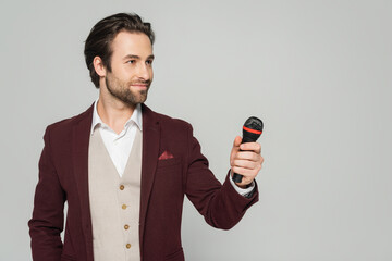 Naklejka premium host of event in red blazer holding microphone isolated on grey