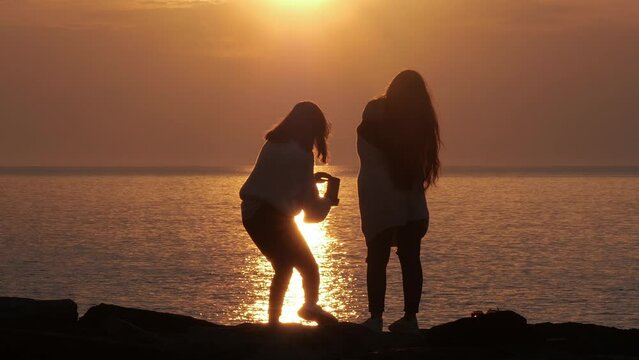 Girls take pictures of themselves at sea at sunset. Two girls are watching the sunset. Two girls watch the sunrise. Dawn on the sea. Sunset on the sea. Selfie on the background of the sea.