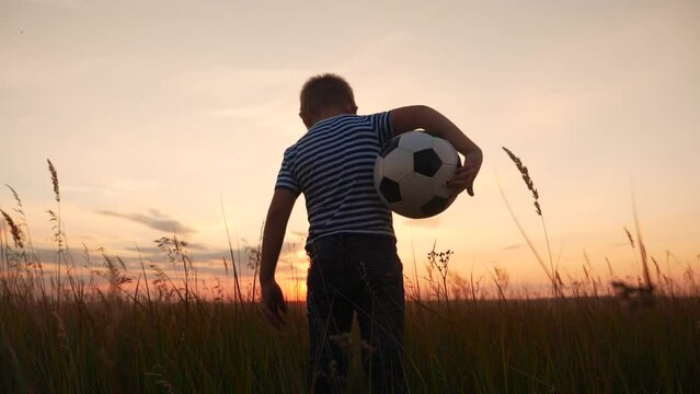 Childhood dream. boy holding soccer ball walking in the park silhouette. happy family kid dream concept. kid boy walking on the field silhouette at sunset carries a soccer ball. baby fun winner