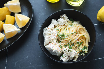 Bowl of spaghetti with ricotta cheese, lemon zest and chopped parsley, horizontal shot on a black marble background