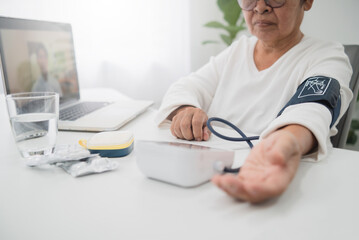 Telemedicine concept, senior asian woman using laptop video call with doctor to use a home blood pressure monitor.