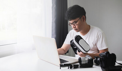 Content Creator for Virtual Reality and Metaverse Concept, Asian man using laptop to edit video, from camera, for VR glasses.