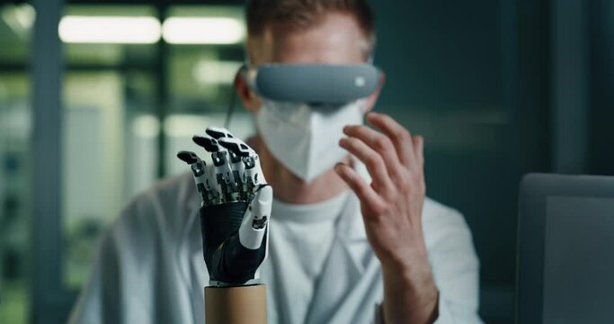 Young Biomedical Engineer is Wearing Virtual Reality Goggles and Controlling Remotely Bionic Limb Prosthesis. Professional Manipulating Artificial Palm. Robotic Innovation for People with Disability.